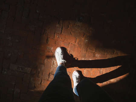 Woman in white sneakers stands in sun beam on old pavement made of red bricks. Modern fashion. Light and shadow.の写真素材