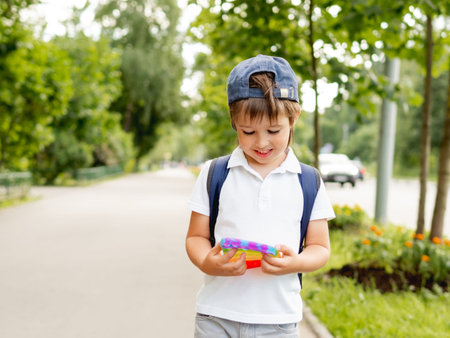 Little boy plays square rubber fidget toy. Rainbow-colored anti stress and tactile toy for all ages. Outdoor recreation with toy for fine motor skills improvement.の写真素材