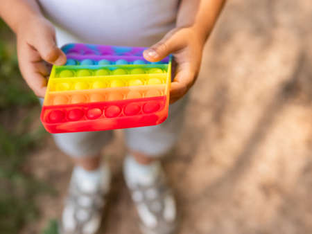 Little boy plays square rubber fidget toy. Rainbow-colored anti stress and tactile toy for all ages. Outdoor recreation with toy for fine motor skills improvement.の写真素材