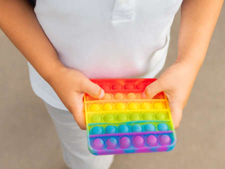 Little boy plays square rubber fidget toy Pop . Rainbow-colored anti stress and tactile toy for all ages. Outdoor recreation with toy for fine motor skills improvement.の写真素材