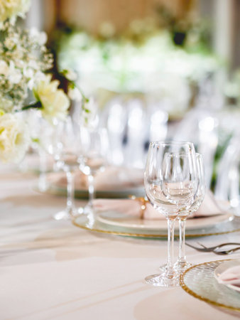 Table serves for banquet. Transparent wine glasses, plates with napkins and shiny cutlery on white table cloth at sunlight.の写真素材