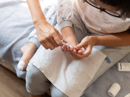 Mother bandages her child's big toe and cuts nails on other foot. Close-up photo of kid's foot with bandaged finger. First aid in case of small domestic injury.の写真素材