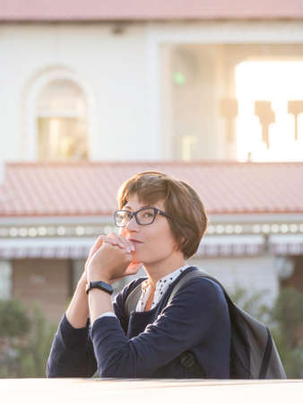Thoughtful woman in eyeglasses leaned against railing. Warm summer sunset in town.の写真素材