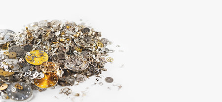 Gears, clock faces and metal parts of internal mechanism of the watch lie in heap on white...