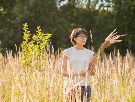 Woman is picking dried grass on autumn field. Florist at work. Using dried plants as decorative bouquet for home interior.の写真素材