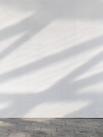 White concrete wall with sunbeams on it. Urban textured wall and tiled pavement. Copy space.