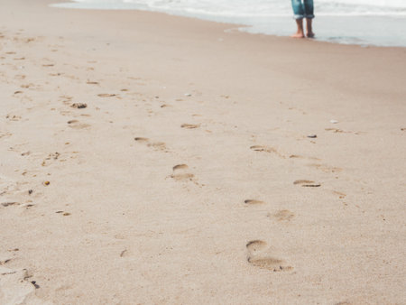Footprints on sandy beach. Man stands alone in soft warm sea surf. Place to relax. Tranquil scene on...