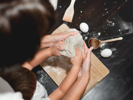 Mother and son are cooking together. Mom and toddler knead dough from flour and eggs on black wooden...