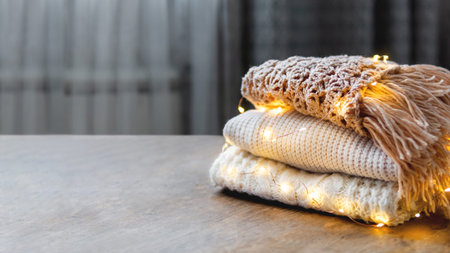 Banner with pile of white and beige cable-knitted sweaters with light bulbs. Copy space on shabby wooden table.の写真素材