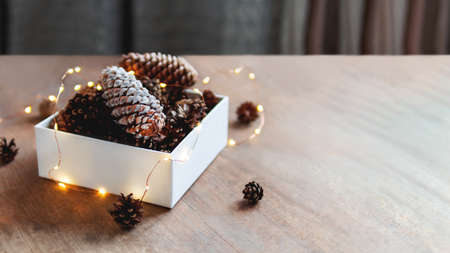 White box with pine cones and light bulbs. Copy space on wooden table. Preparation for Christmas and New Year celebration.の写真素材