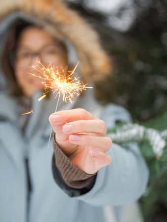 Smiling woman celebrates Christmas or New Year with bright sparkler. Bengal fire, traditional...