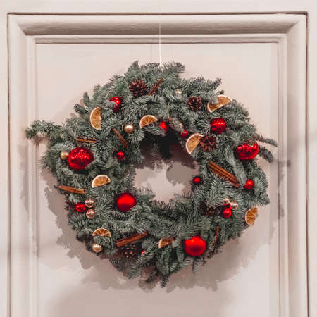 Christmas wreath made of fir tree branches, pine cones, bright red balls, dried lemon and cinnamon. Round decoration for New Year celebration.の写真素材
