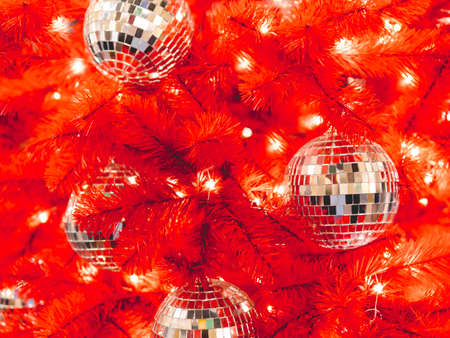 Red artificial Christmas tree with mirror disco balls. Bright fir tree decorated with light bulbs for New Year celebration.の写真素材