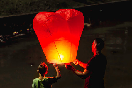PHUKET, THAILAND - November 28, 2012. Man and boy release heart shaped chinese flying lantern....