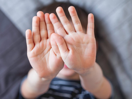 Little boy covers his face with hands. Child refuses to be photographed. Playful kid shows his palm hands instead of laughing face.の写真素材