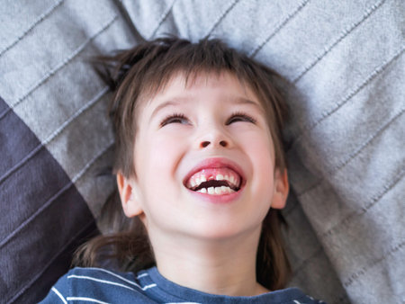 Laughing kid shows hole in row of teeth in his mouth. One incisor fell out just now. Close up photo...
