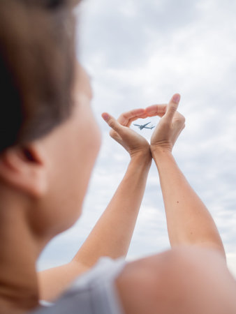 Woman makes heart symbol with flying plane in it. Romantic gesture of wanderlust. Travel by plane concept.の写真素材