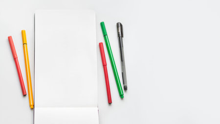 Top view on clear page of notebook. Mock up photo with notepad and colorful markers on white table....