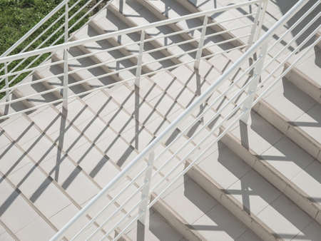 White exterior of outdoor staircase with railing. Sunlight and shadow on stone steps. Urban geometry.の写真素材