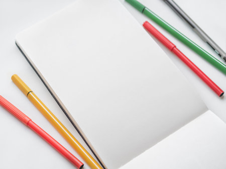 Top view on clear page of notebook. Mock up photo with notepad and colorful markers on white table....