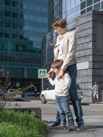 mother and son stand on street in sunlight. Woman and kid in modern town with transport traffic and road sign. family in city.の写真素材