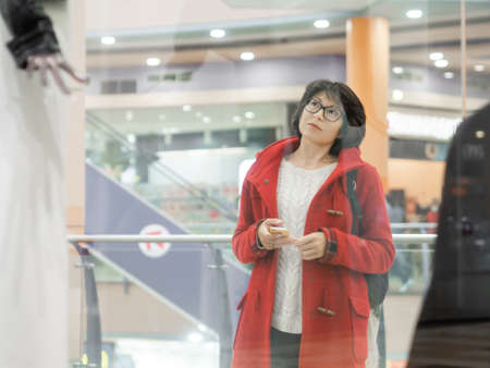 Woman stares on dummies in clothing store. Casual outfit hanging on mannequins. View through transparent shop window. Shopping at mall. Basic clothes for everyday wear. Modern urban fashion.の写真素材