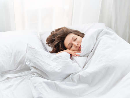 Caucasian woman is sleeping in bed. Healthy sleep on white bed linen. Morning at cozy home.の写真素材