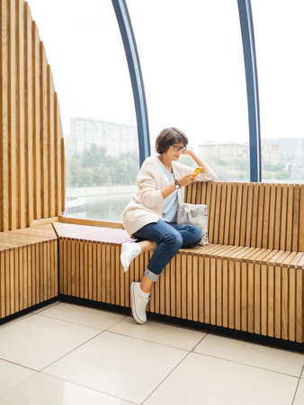 Mindful woman in eyeglasses is texting in smartphone. Casual wear woman with gadget. Millennial lifestyle.の写真素材