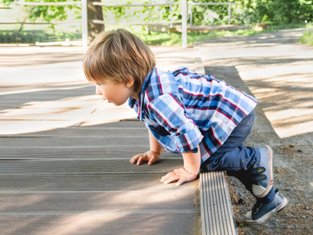 Curious toddler is climbing upstairs in recreation park. Leisure activity for little children. Kid explores everything around him. Physical development of children.の写真素材