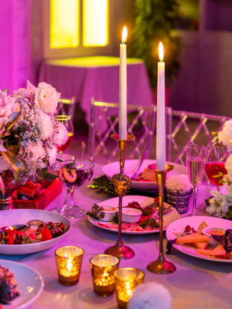 Table served for banquet or romantic date with candles and floral compositions. Beautiful decorations in pink electric light.の写真素材