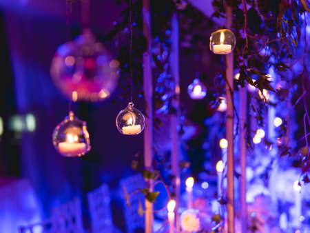 Candles in small glass circlular candle holders handled on strings. Beautiful decorations in blue electric light.の写真素材