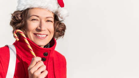 Curly winking woman with striped candy cane. Pretty female with Christmas licorice whip. Banner with copy space.の写真素材