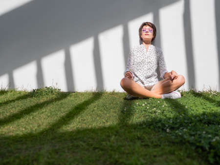 Woman is meditating on lawn in urban park. nature in town. Relax outdoors after work. summer vibes.の写真素材