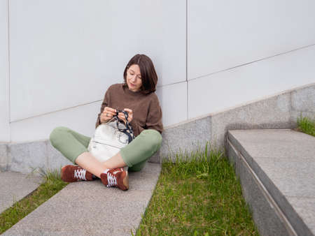 Woman is crocheting outdoor. Tranquil leisure of female in urban park. Anti stress hobby.の写真素材