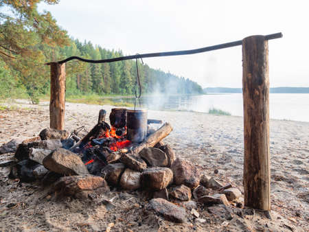 Cooking in pot over fire. Touristic camp on sandy beach of Kenozero lake. Camping and hiking in Karelia, Russia.の写真素材