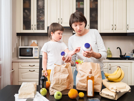 Woman and toddler boy sorts out purchases and reads names on bottles with vitamins in the kitchen. Mother and son with grocery delivery in paper bags.の写真素材