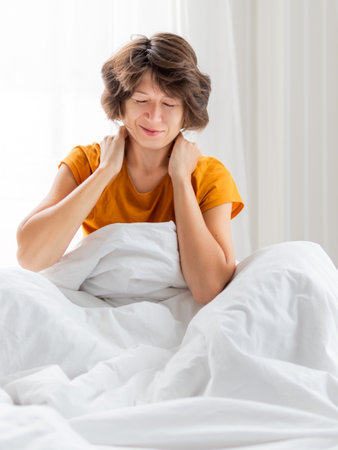 Sleepy woman in yellow pajama is massaging her neck. Waking up early in the morning. Woman gets enough sleep.の写真素材