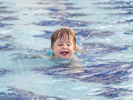 Toddler floats in paddling pool. Teaching children to swim from early childhood. Sport, active lifestyle and physical development.の写真素材