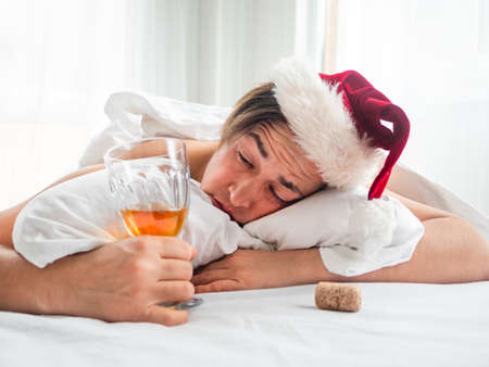 Man in Santa hat is trying to freshen the nip after alco party. He is suffering of headache after New Year or Christmas celebration. Heavy morning. Alcohol withdrawal. Worst hangover.の写真素材