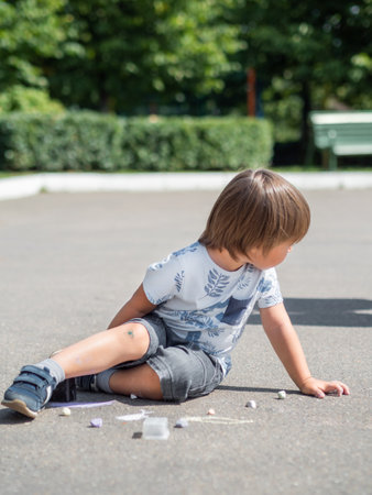 Little mindful kid sits on pavement in park. Kid is drawing something on asphalt. Creative leisure activity for children.の写真素材