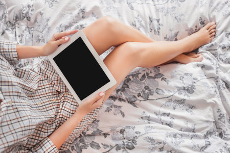 Top view on woman in pajamas with digital tablet. Checking e-mail and reading news on gadget in bed. Clear black screen of electronic device. copy space or mock up.の写真素材