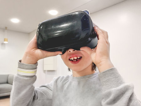 Smiling boy is watching something in VR-glasses. New technology for entertainment and developing skills. Device with usage of smartphone and application.の写真素材