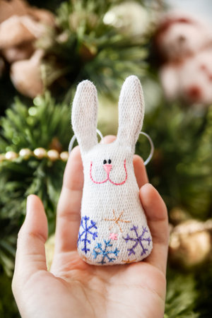 Woman holds cute handmade rabbit with embroidered snowflakes. DIY decoration for Christmas tree. Present or souvenir, symbol of New Year 2023 year.の写真素材