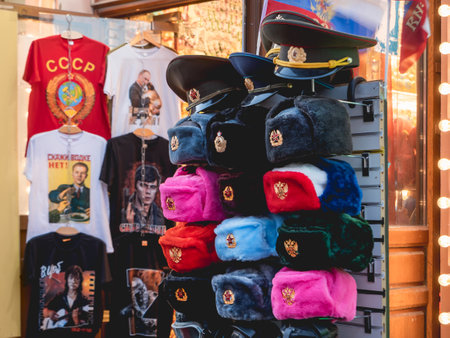 MOSCOW, RUSSIA - October 16, 2022. Souvenir shop on Arbat street. Sale of colorful furry military hats with old USSR emblem, t-shirts with prints and quotes.のeditorial素材