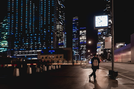 MOSCOW, RUSSIA - November 11, 2022. Young man stands in lantern light under street clocks. Bus stop near Moscow-city International Business Center.のeditorial素材