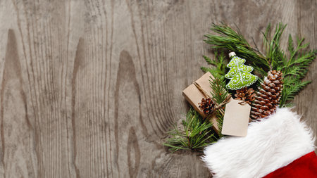 Christmas presents in Santa Claus red sock with natural coniferous branches as decoration. Top view, flat lay on wooden table. New Year gifts. Banner with copy space.の写真素材