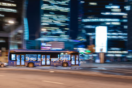 MOSCOW, RUSSIA - November 11, 2022. Electric bus is moving fast on urban road among skyscrapers. Blurred illumination of towers Moscow International Business Center.のeditorial素材