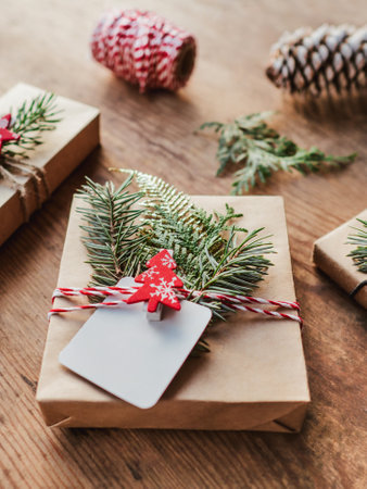 Christmas DIY gifts in craft paper with fir tree twigs. Red decorations in shape of Christmas tree, stars. New Year gifts on wooden table. Winter holiday spirit. clear label. copyspace.の写真素材