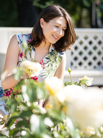 Woman is admiring of blooming roses in public park. summer vibes. Tropical plants and flowers in bloom in garden. Floriculture as hobby.の写真素材