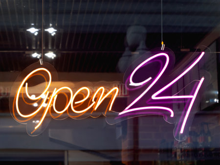 Glowing ad is OPEN 24 hours a day in cafeteria window. Modern electric signboard to attract attention of passers-by. Dark interior and colorful illuminated sign.の写真素材